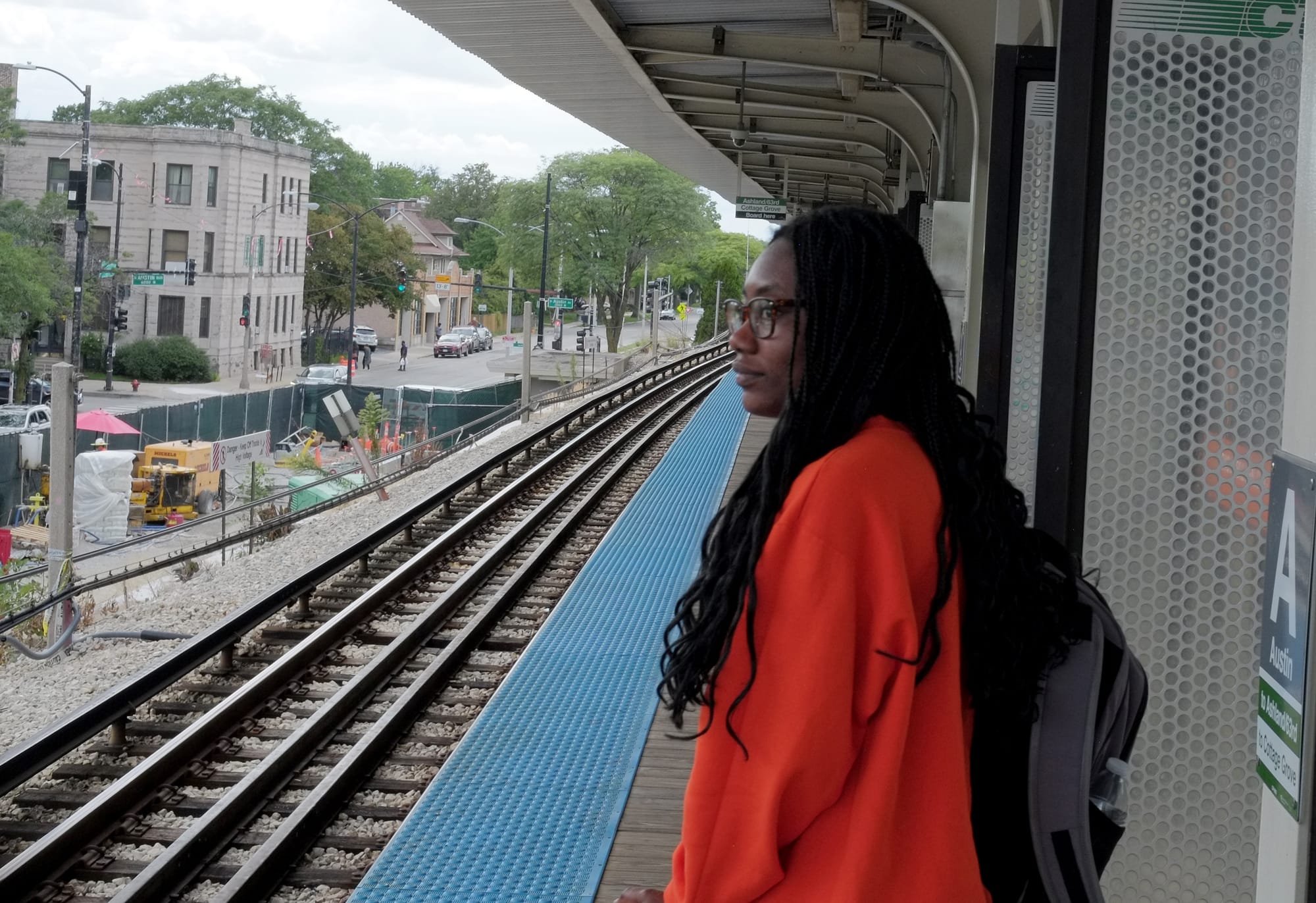 A woman in a bright orange sweatshirt is shown waiting for a downtown bound Green Line train at the Austin station. 