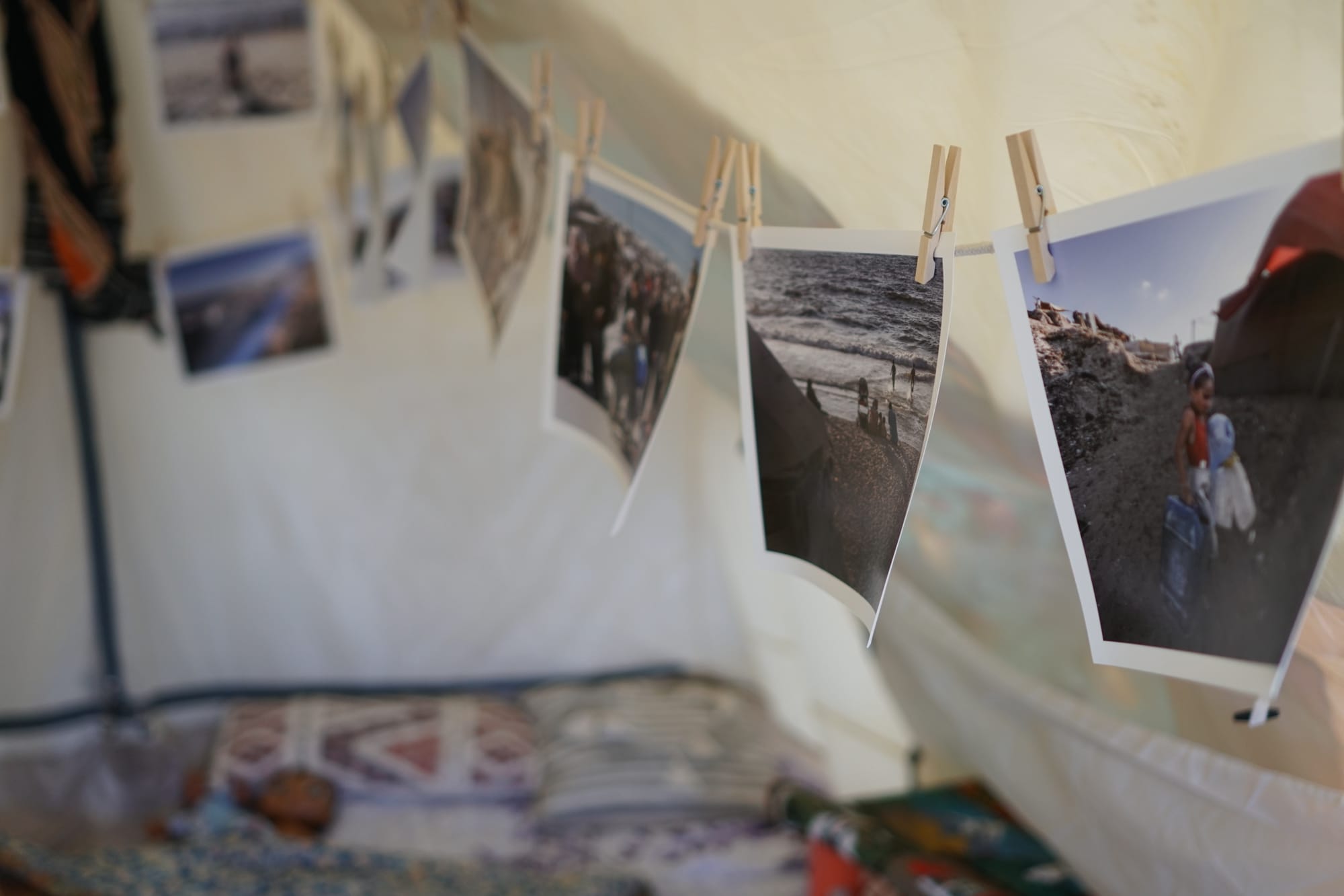Several photographs clipped to a clothesline with wooden clothespins, showing various scenes including ocean views and people at a beach. Additional photos are visible in the background on what appears to be a desk or table surface.