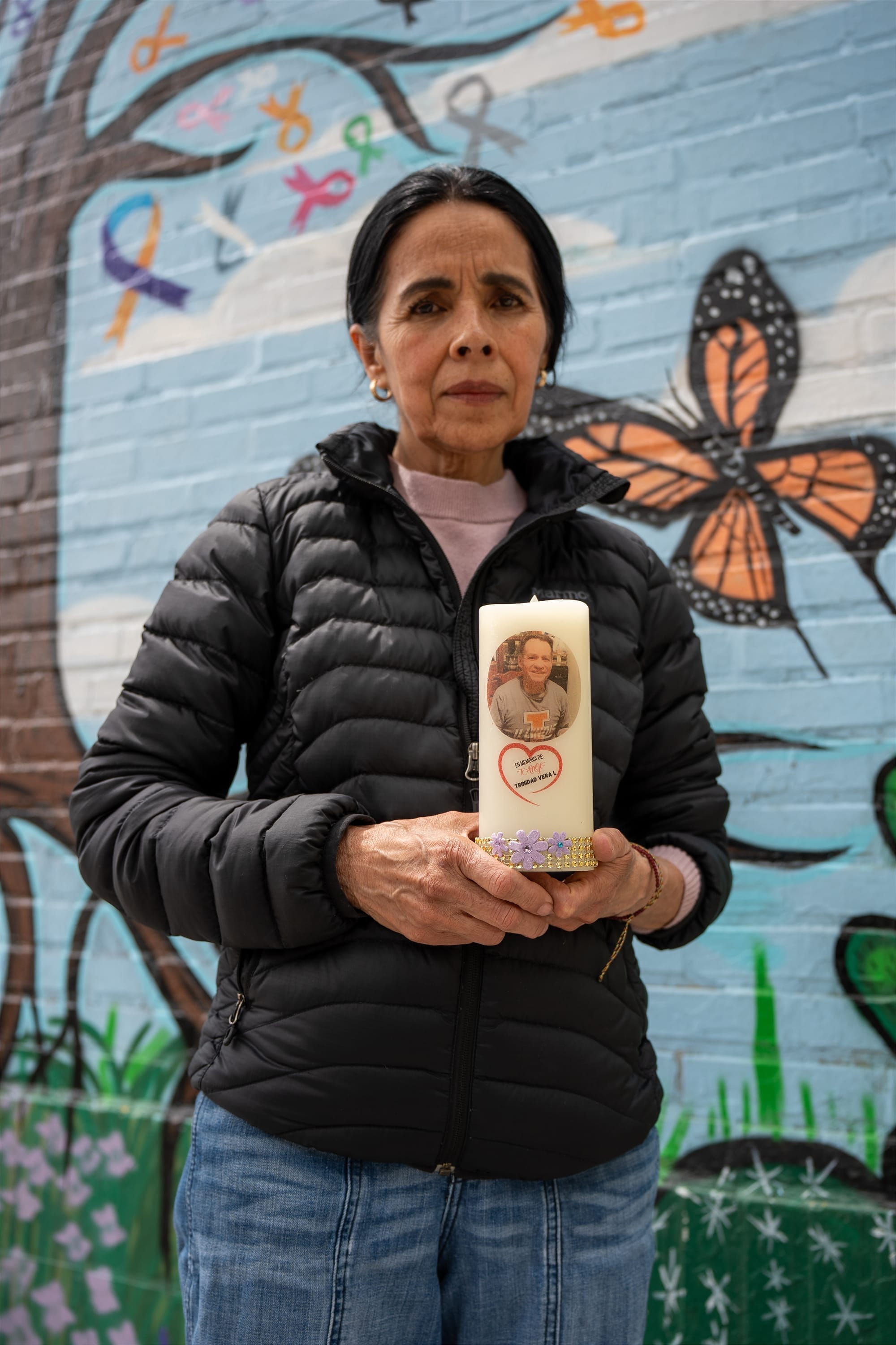 Dolores Castañeda holds a memorial candle honoring her late brother, Jose Trinidad Vera, in front of the mural in Little Village on May 5, 2026. | Araceli Ramirez/15 West