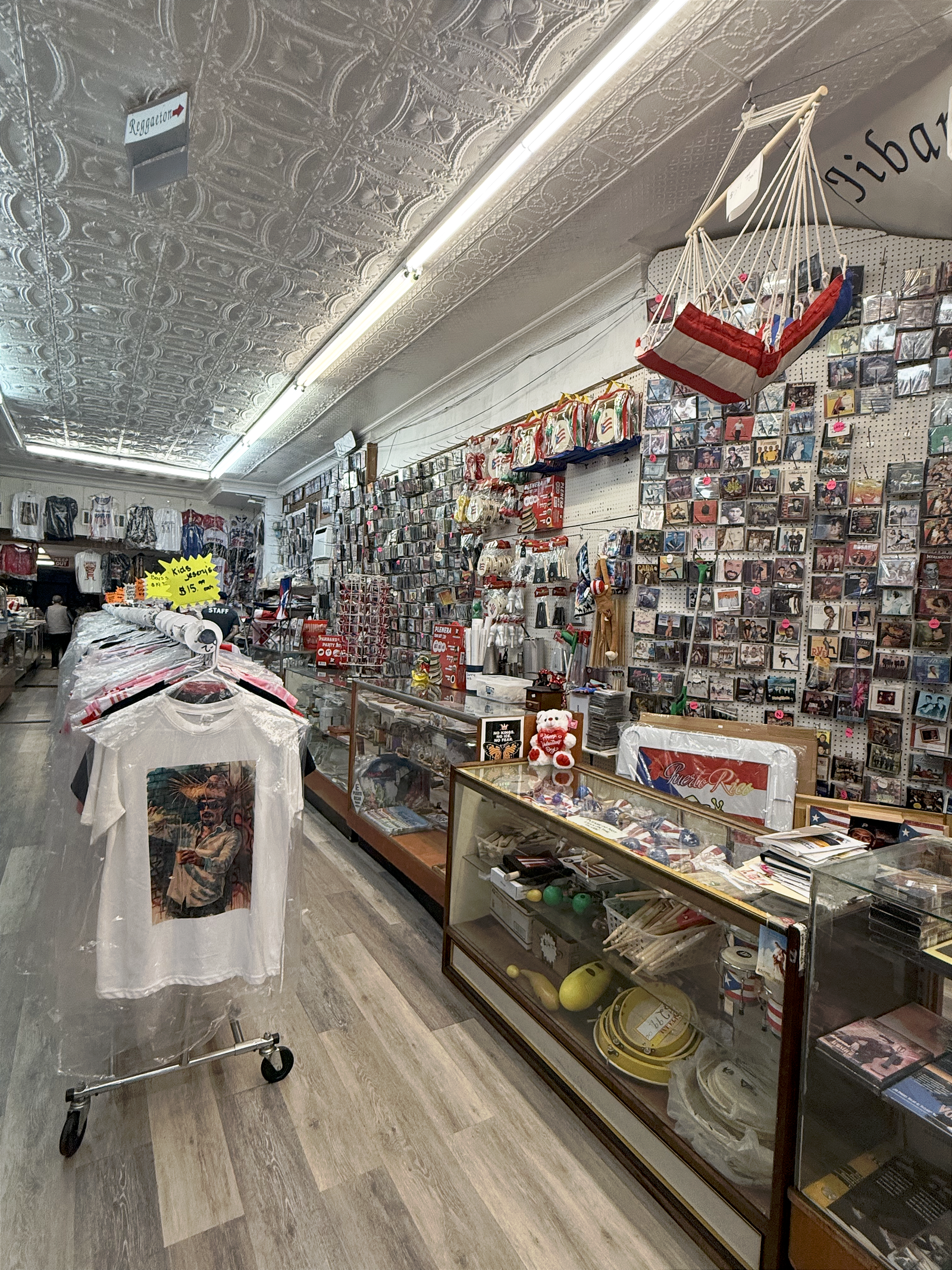 Foto más amplia donde se muestra la tienda. La tienda tiene polos, CDs en las paredes, tambores pequeños, recuerdos de Puerto Rico, etc.
