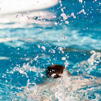 A child is splashing in a pool. His head can be seen just over the surface of the water