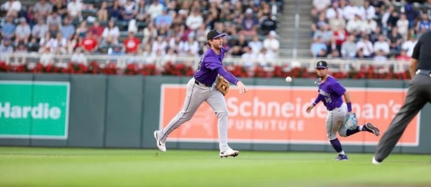 McMahon throws a baseball while Tovar looks on. They’re wearing purple jerseys.