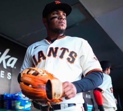 Thairo Estrada stands in the Giants dugout holding his glove.