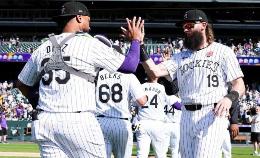 Both players are wearing purple pinstripes and black caps. Díaz has on his catcher’s gear.