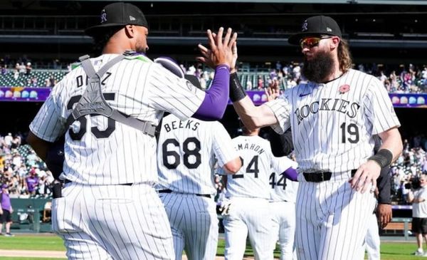 Both players are wearing purple pinstripes and black caps. Díaz has on his catcher’s gear.
