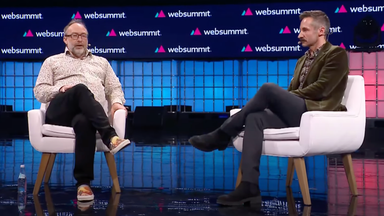 Jimmy Wales (à esquerda) e Ryan Heath (à direita) no palco da Web Summit 2023 sentados em cadeiras.