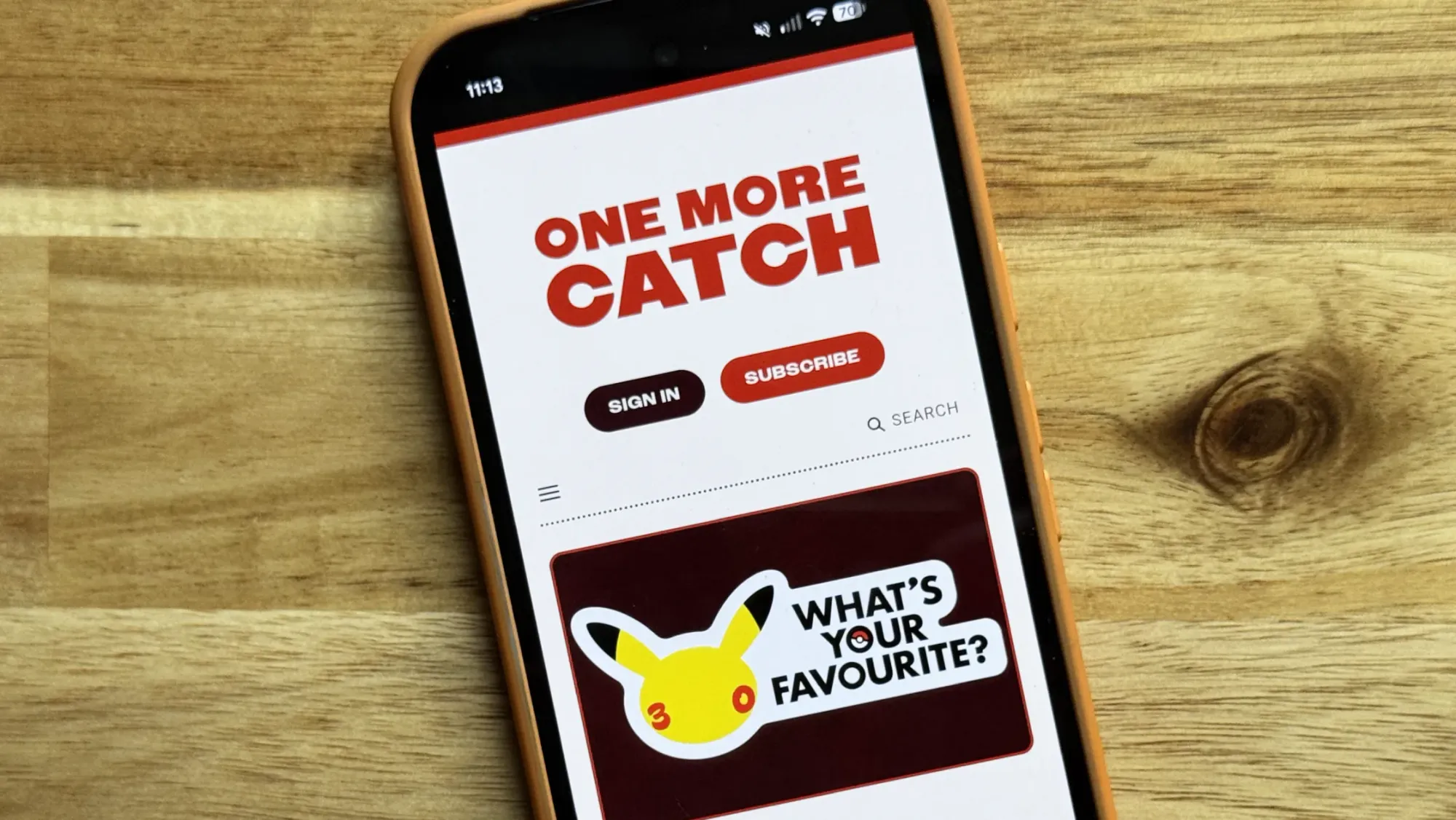 A phone on a table showing the One More Catch homepage.