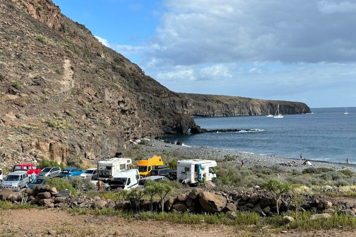 Small Car Park At Playa Del Medio La Gomera With Rocky Beach And Blue Sea And White Sailing Boats In The Background One Of The Best La Gomera Beaches 