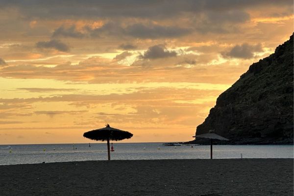 A Sandy Volcanic Beach At Sunset With Rocky Cliffs And Umbrella Shades At Playa De San Sebastian 