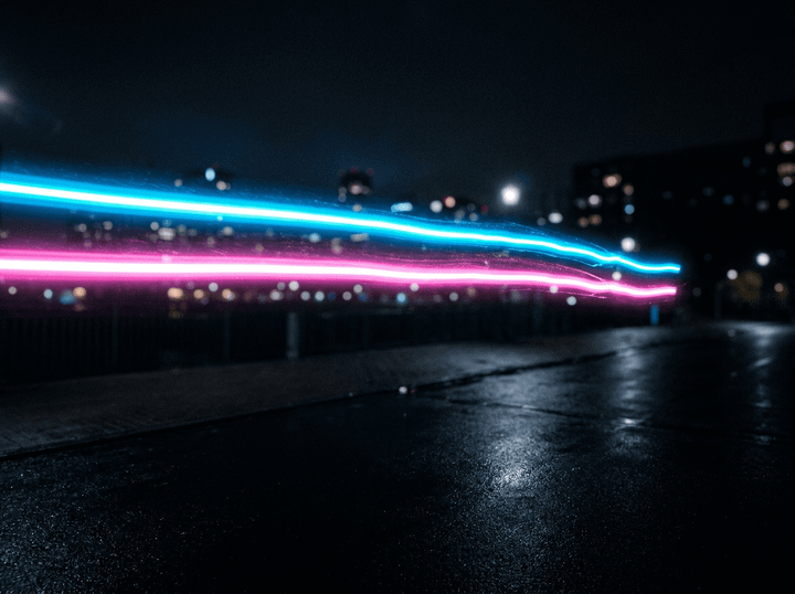 Cyan and pink neon light trails above a wet city street at night