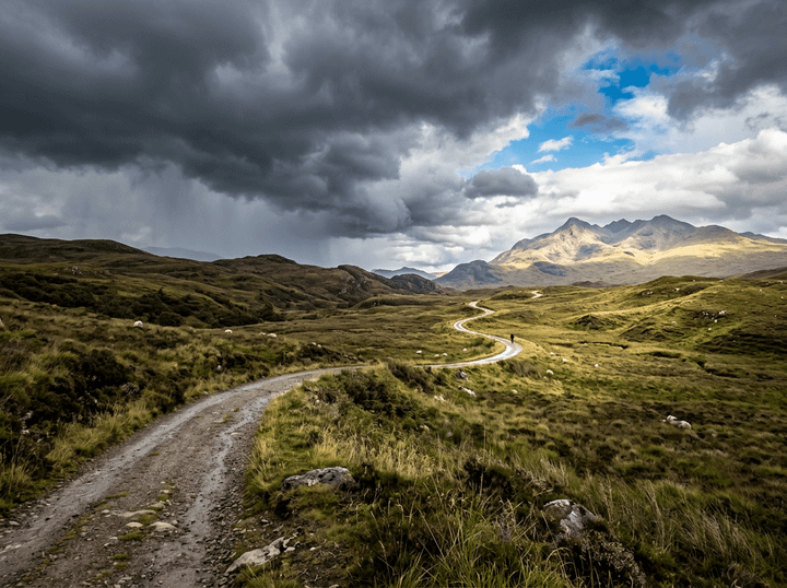 Winding gravel path through grassy hills with storm clouds and sunlit mountains
