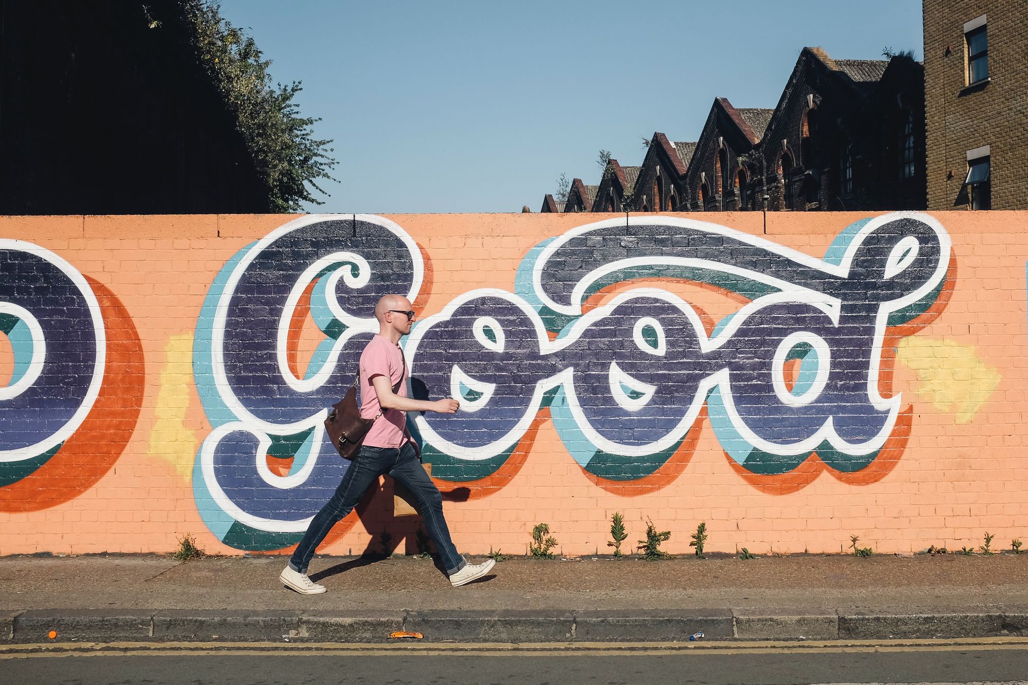 Man in pink t shirt walking beside a graffitti wall that reads "Good"