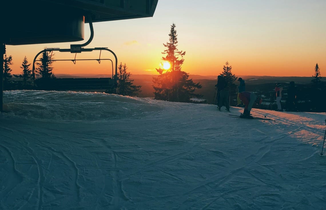Skiers getting off a chairlift with the sun setting in the background