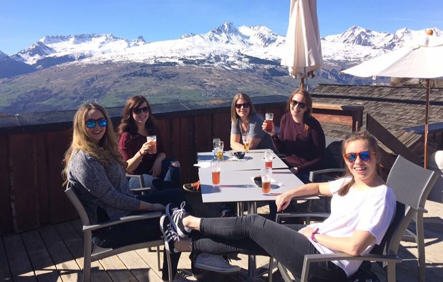 Iglu Ski team sitting on balcony with cocktails and mountain scenery in background