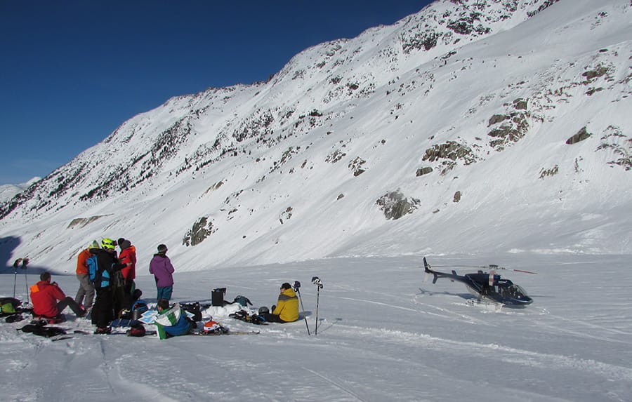 Group of skiers sat on mountain next to parked helicopter