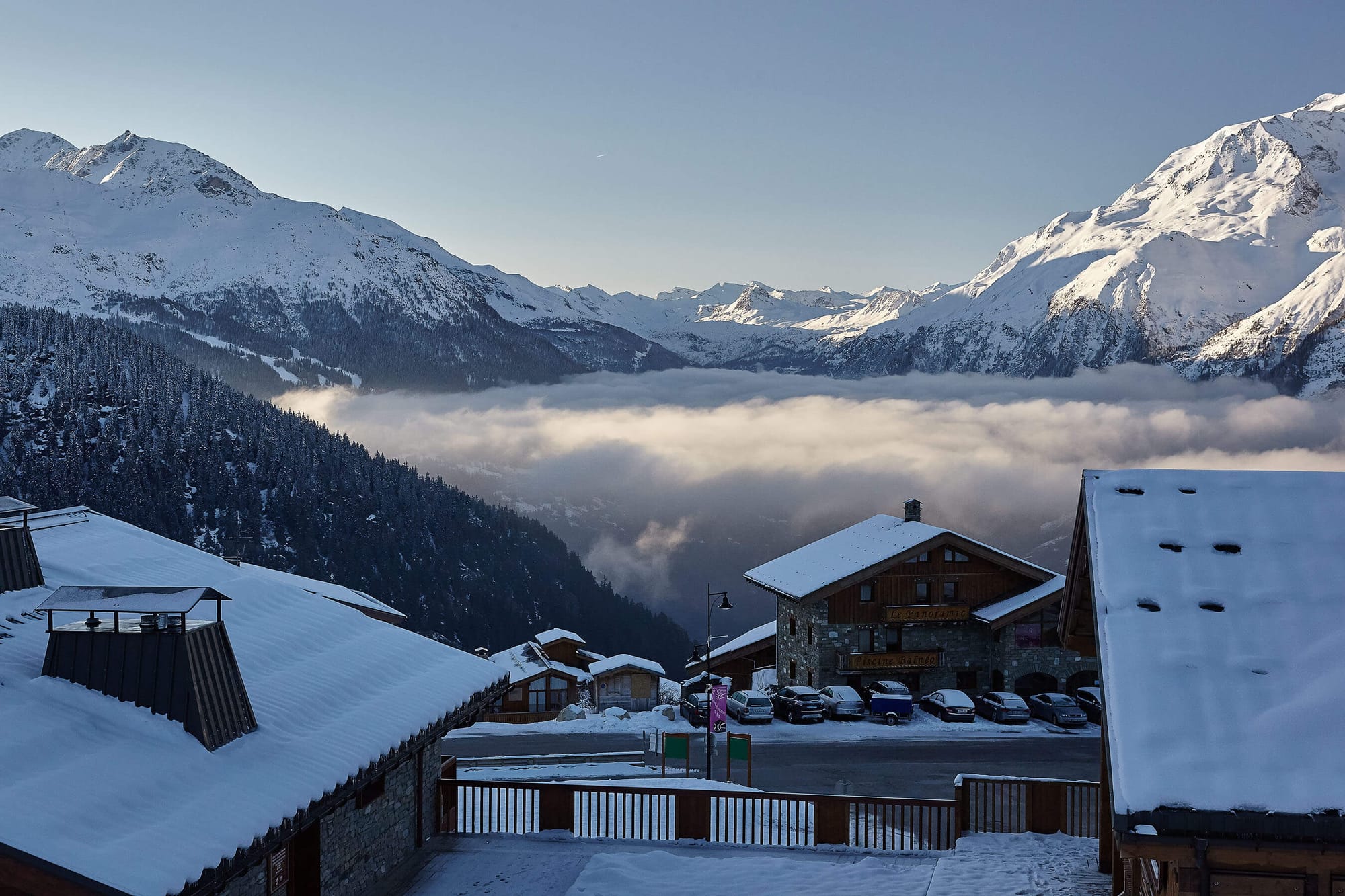 Looking out over low cloud and the mountains from a resort building with a line of cars in the foreground.