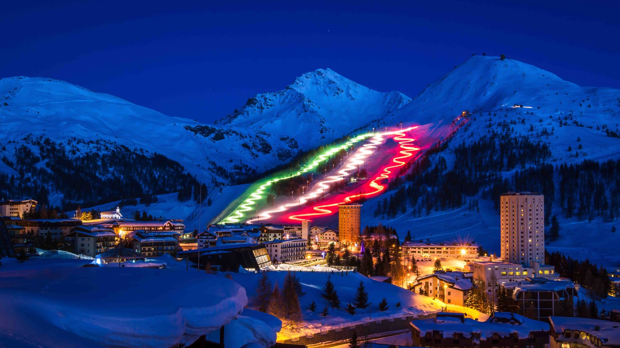 Skiers go down slope leading into Sestriere at night time