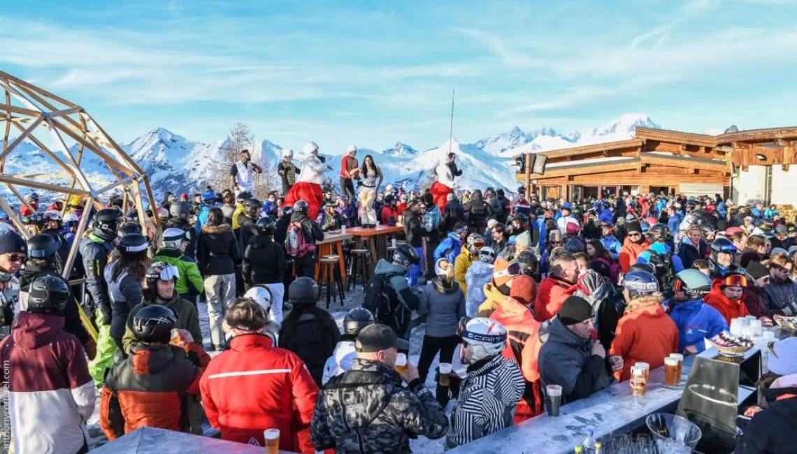 Dancer on table and people enjoying sun terrace of L'Arpette in Les Arcs with magnificent mountain backdrop