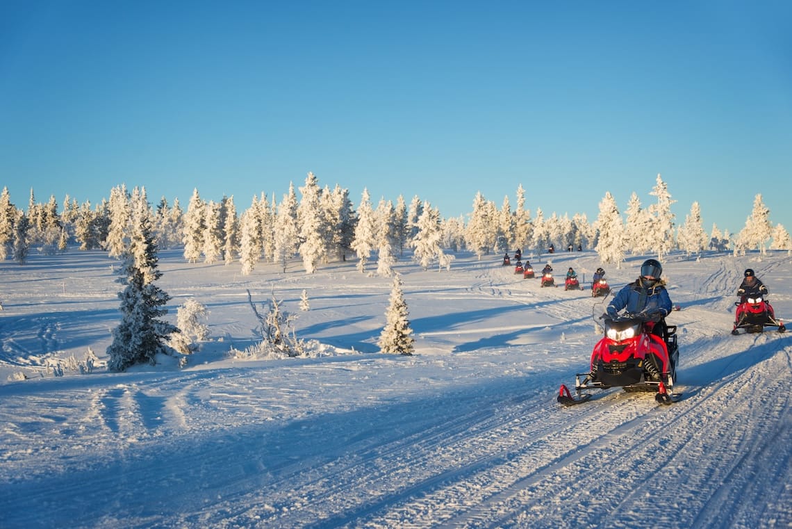 A group rides red snowmobiles in the snowy Lapland wilderness