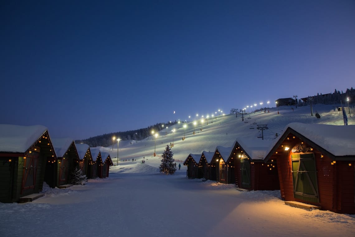 Lit up wooden huts at the bottom of an illuminated ski slope in Levi, Lapland