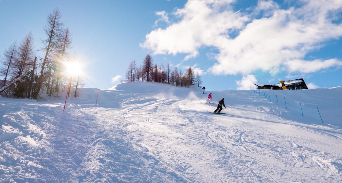 Skiers descend piste on sunny day in Sauze D'Oulx, Italy