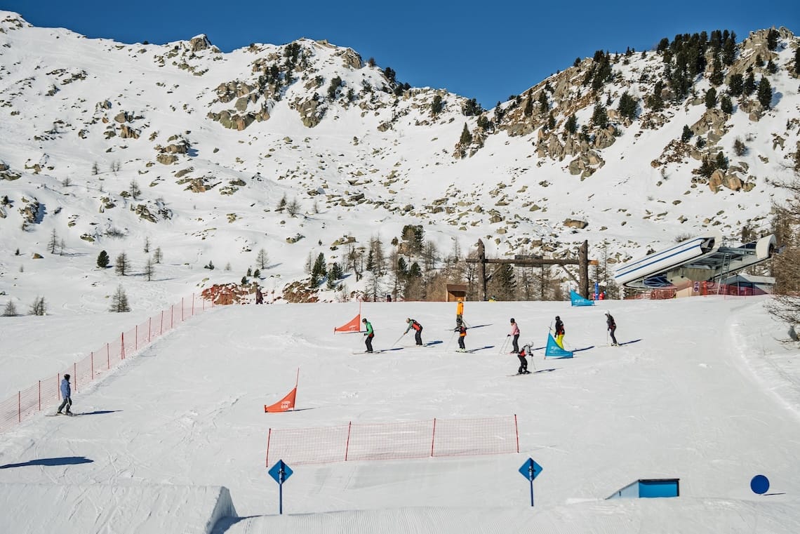 A group of adults learn to ski against a snowy mountain backdrop