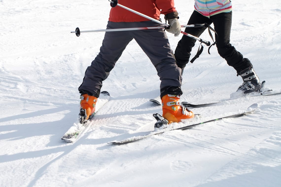 An instructor leads a beginner skier in a snow plough