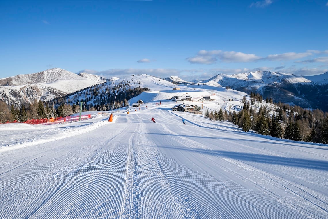 Two skiers on a freshly-groomed piste in Bad Kleinkirchheim under blue skies