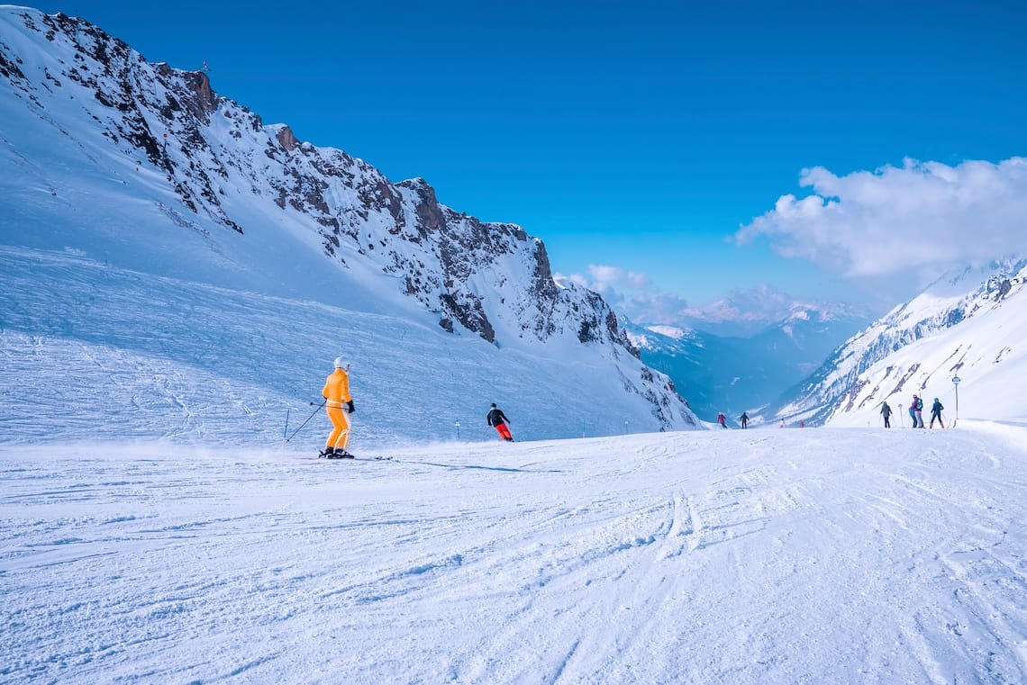 People in ski wear sliding down slope on snowy mountain at ski resort during beautiful sunny day, Skiers skiing downhill on snowy mountain