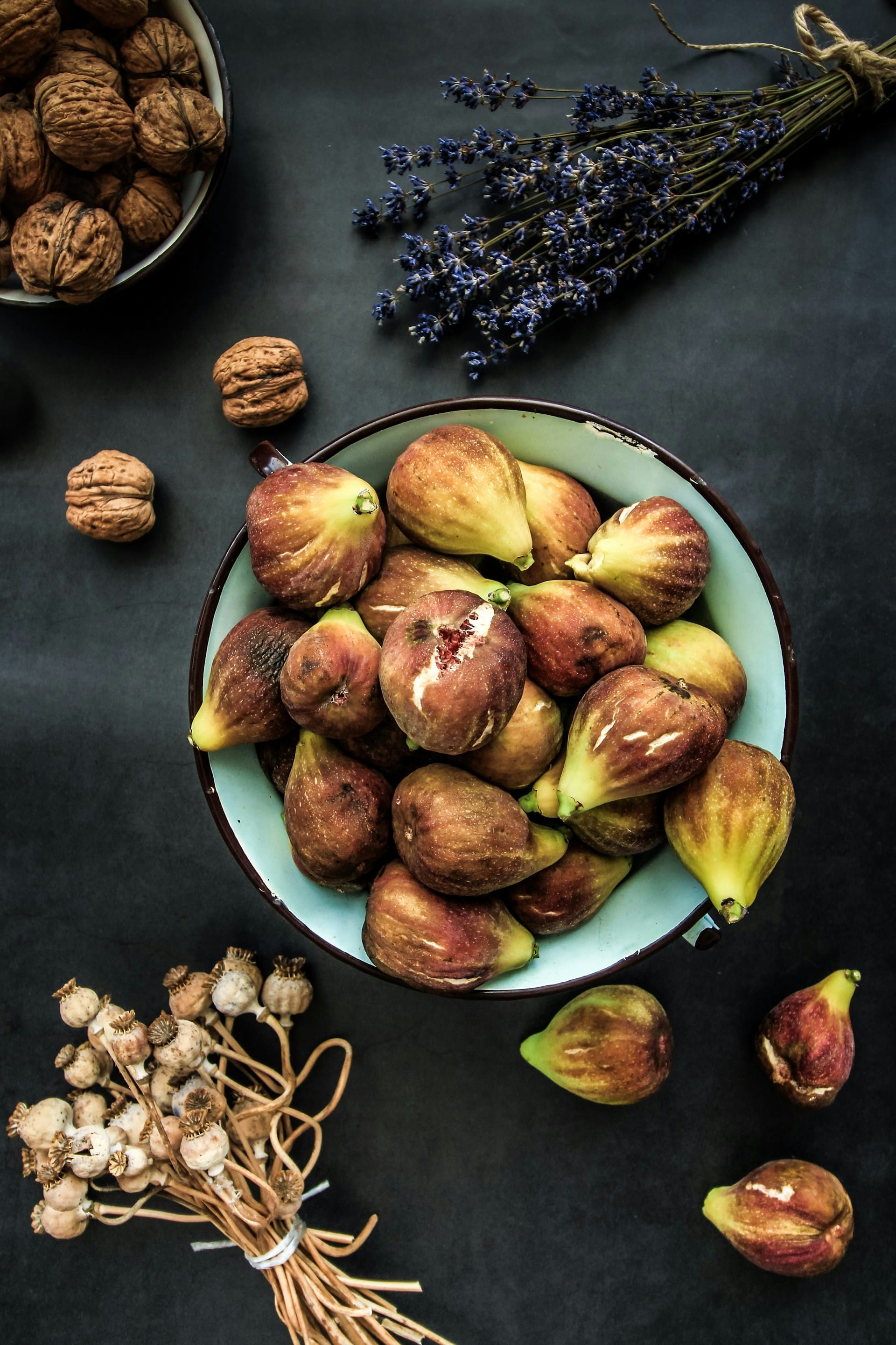 Freshly harvested whole foods including figs, walnuts, poppies, and lavender arranged on a rustic wooden table.