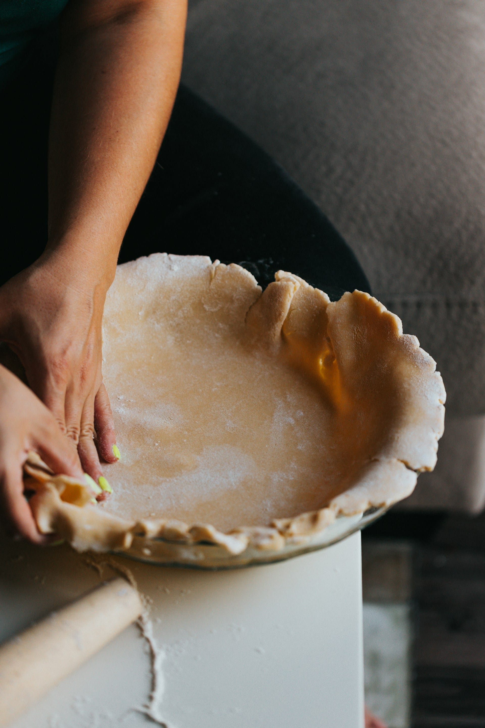 Hands gently fitting rolled-out pastry dough into a glass pie dish on a flour-dusted counter.