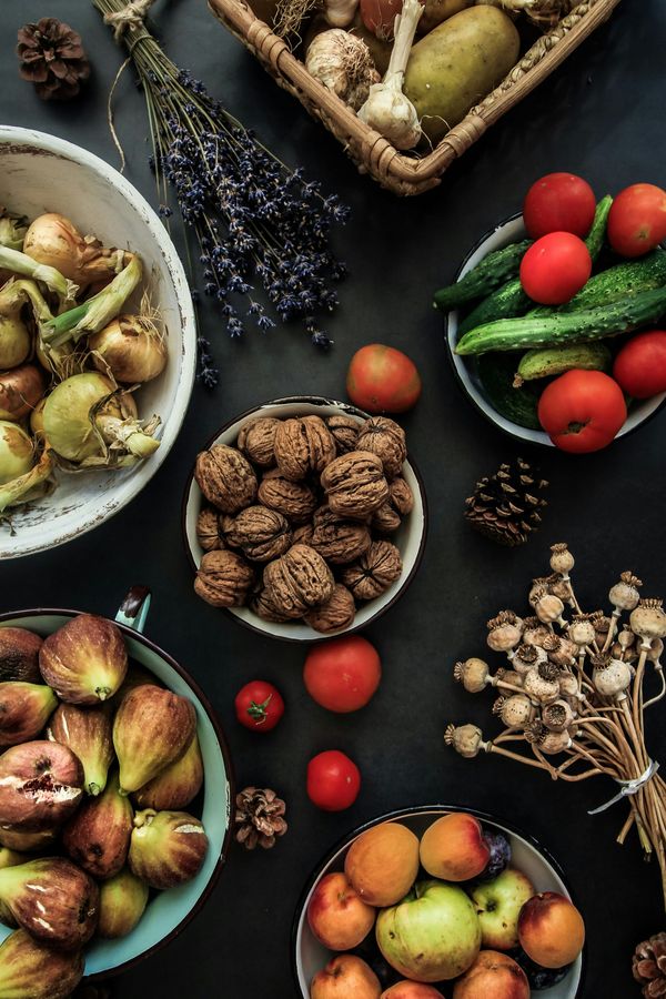 Freshly harvested whole foods including tomtoes, cucumbers, figs, walnuts, and onions arranged on a rustic wooden table.