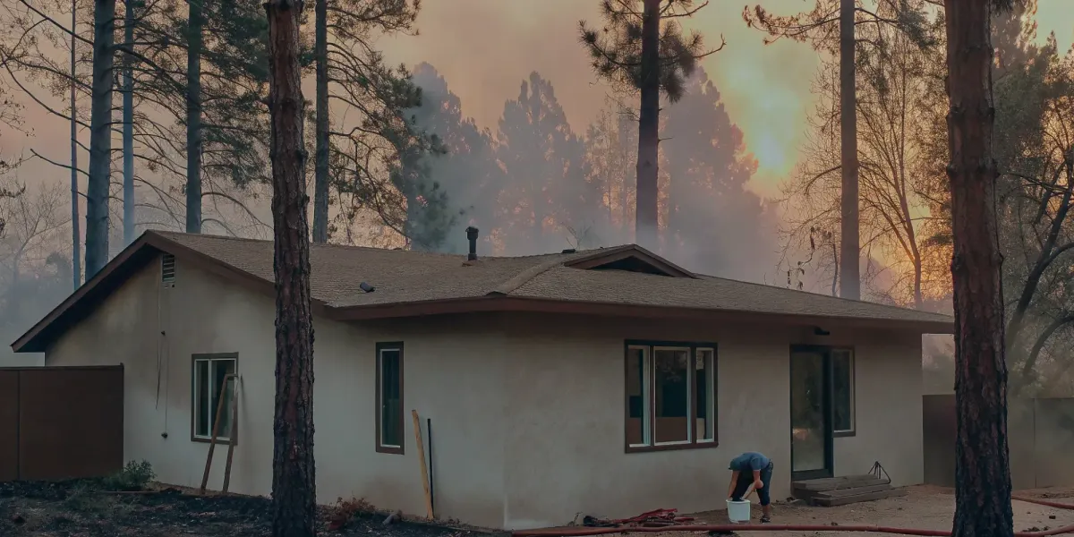 Homeowner preparing a house for a wildfire using a proofing checklist as smoke appears in the background.