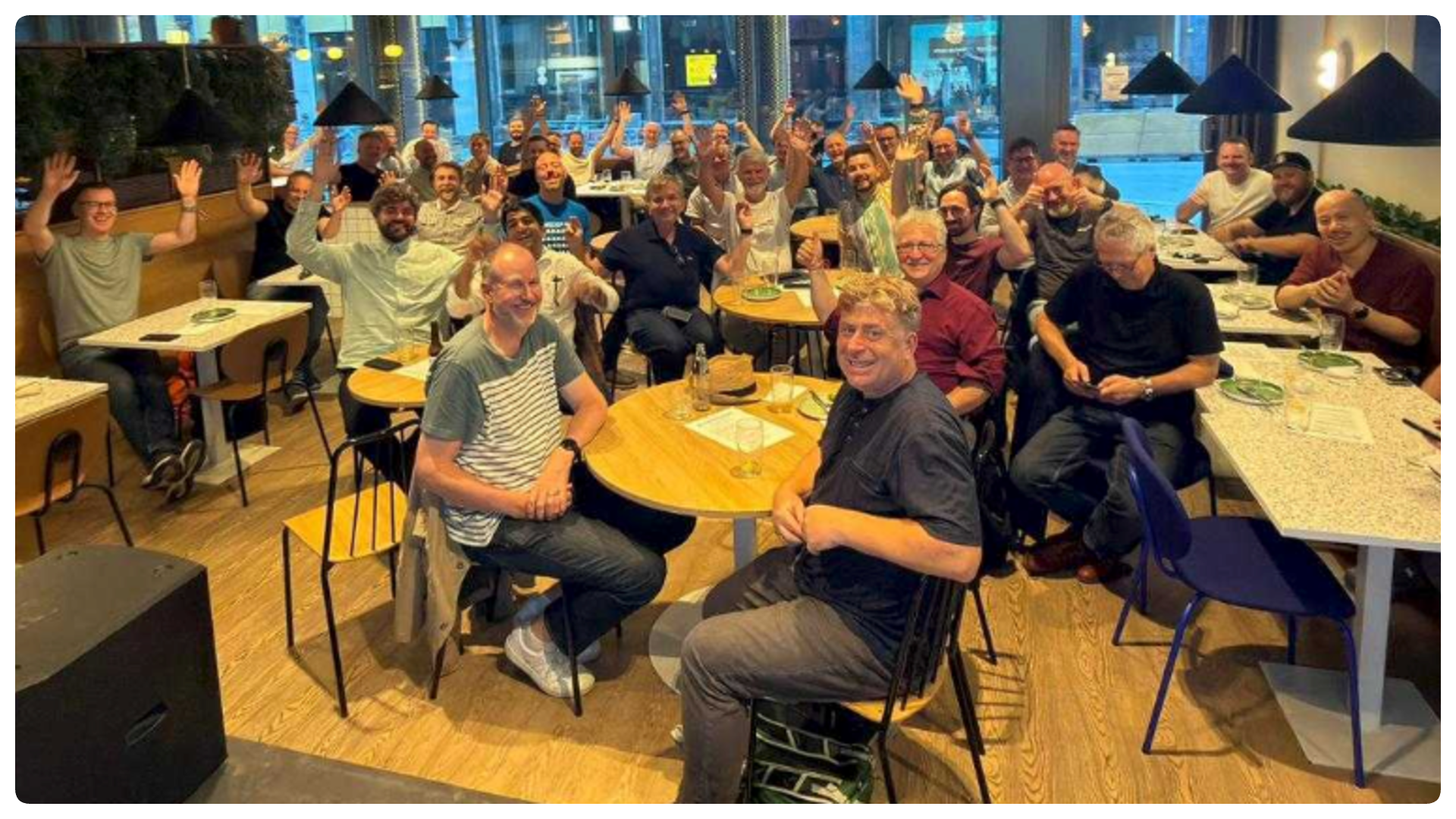 A group of people sitting down waving their hands and smiling at the camera at the Home Assistant meetup in Oslo.