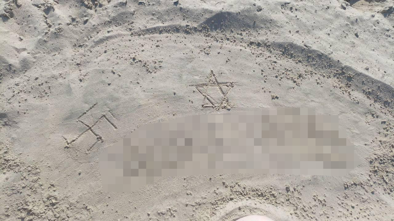 Two simple symbols are carved in beach sand: A Swastika (left) and Star of David (right). Text below these is blurred.