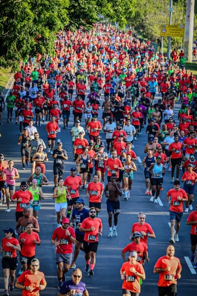Corredores ocupa toda a avenida durante a corrida de rua do Circuitos das Estações- Etapa Verão no Rio de Janeiro. A maioria dos corredores vestem camisetas vermelhas com número de peito. Já outros, vestem camisetas da cor verde, roxa, azul, acompanhadas também do número de peito.
