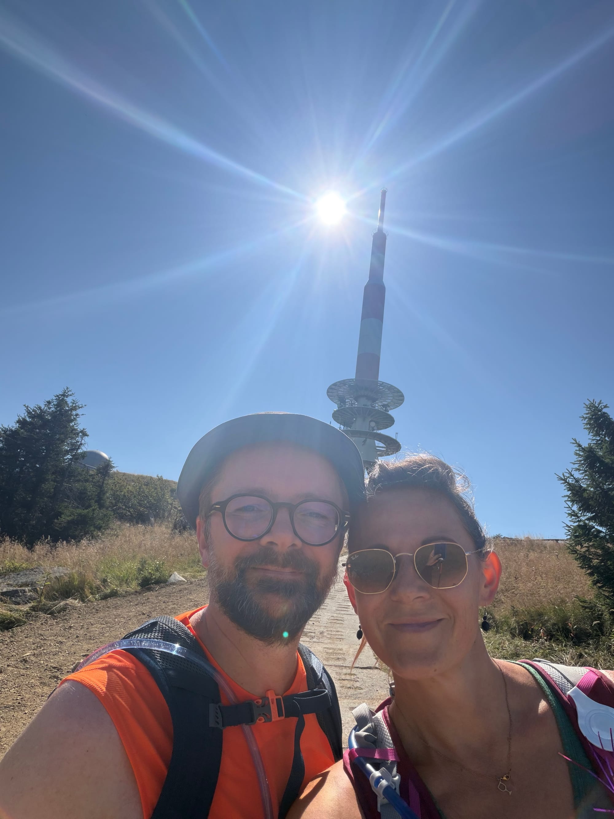 elfie von Roman und Nicole bei strahlendem Sonnenschein auf dem Brockenplateau vor dem großen rot-weißen Sendemast. © Nicole Isensee
