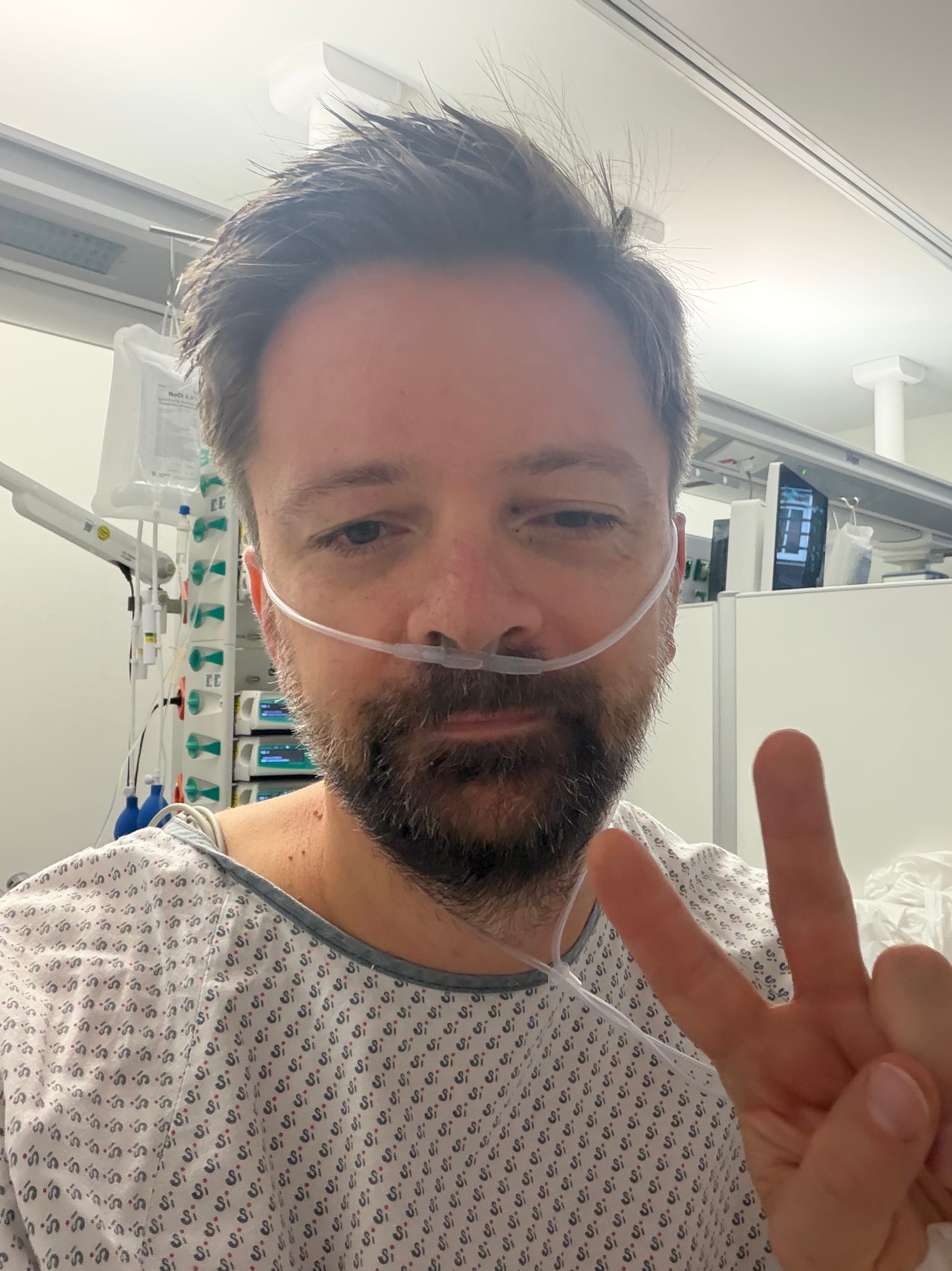 Selfie von Roman Jasiek im Krankenhaushemd auf der kardiologischen Station mit einer Sauerstoffbrille in der Nase und einem Peace-Zeichen. © Roman Jasiek