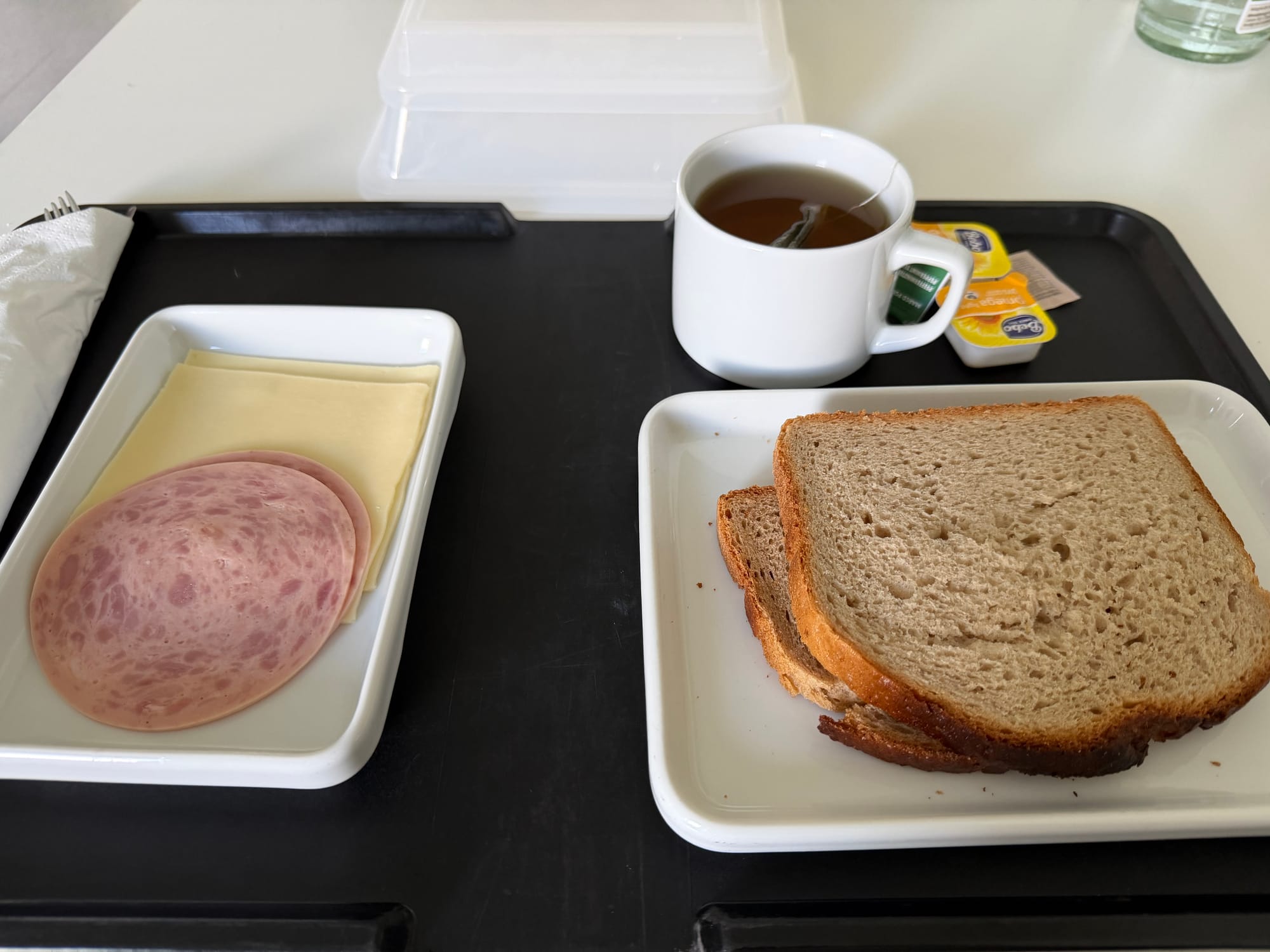 Ein typisches Krankenhaus-Abendessen auf einem schwarzen Tablett mit zwei Scheiben Graubrot, Käse, Wurst und einer Tasse Tee. © Roman Jasiek