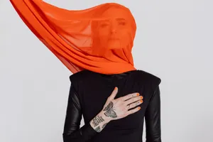 Pressefoto „Poesie & Widerstand" von Sarah Lesch im Querformat: Künstlerin mit orange-transparentem Schleier und tätowierter Hand (© Sandra Ludewig)