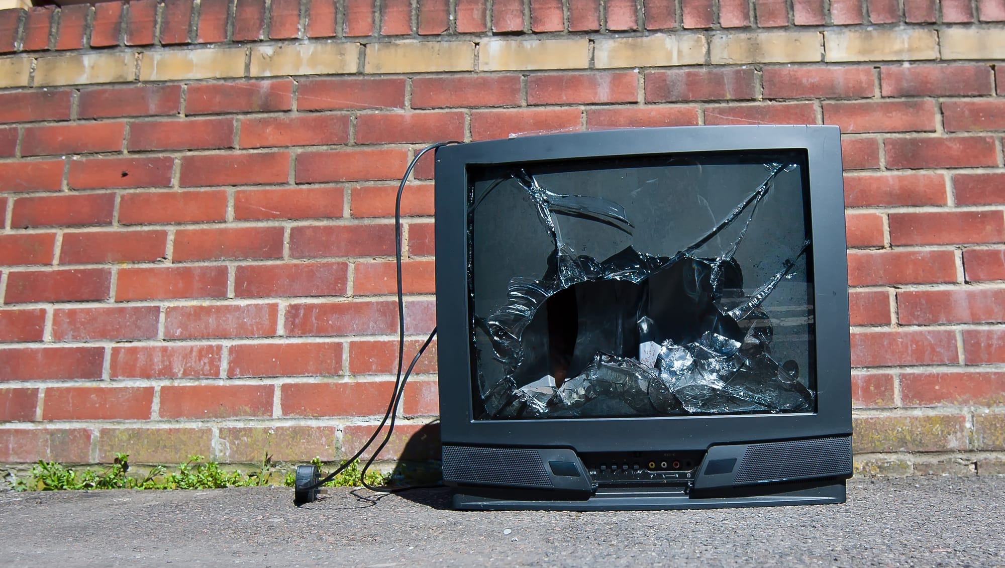 A smashed television sits on a city sidewalk, waiting for the trash collector.