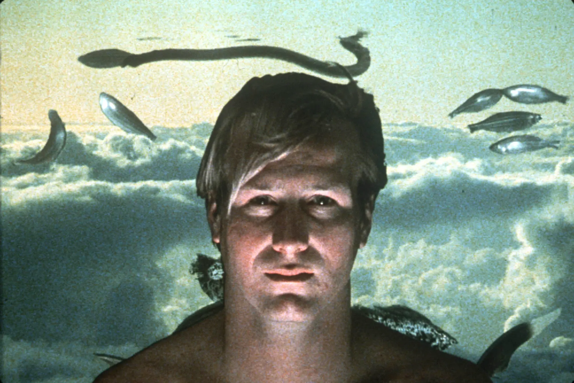 A man gazes quixotically into the camera while behind him hover dreamy images of clouds, fish, and snakes.