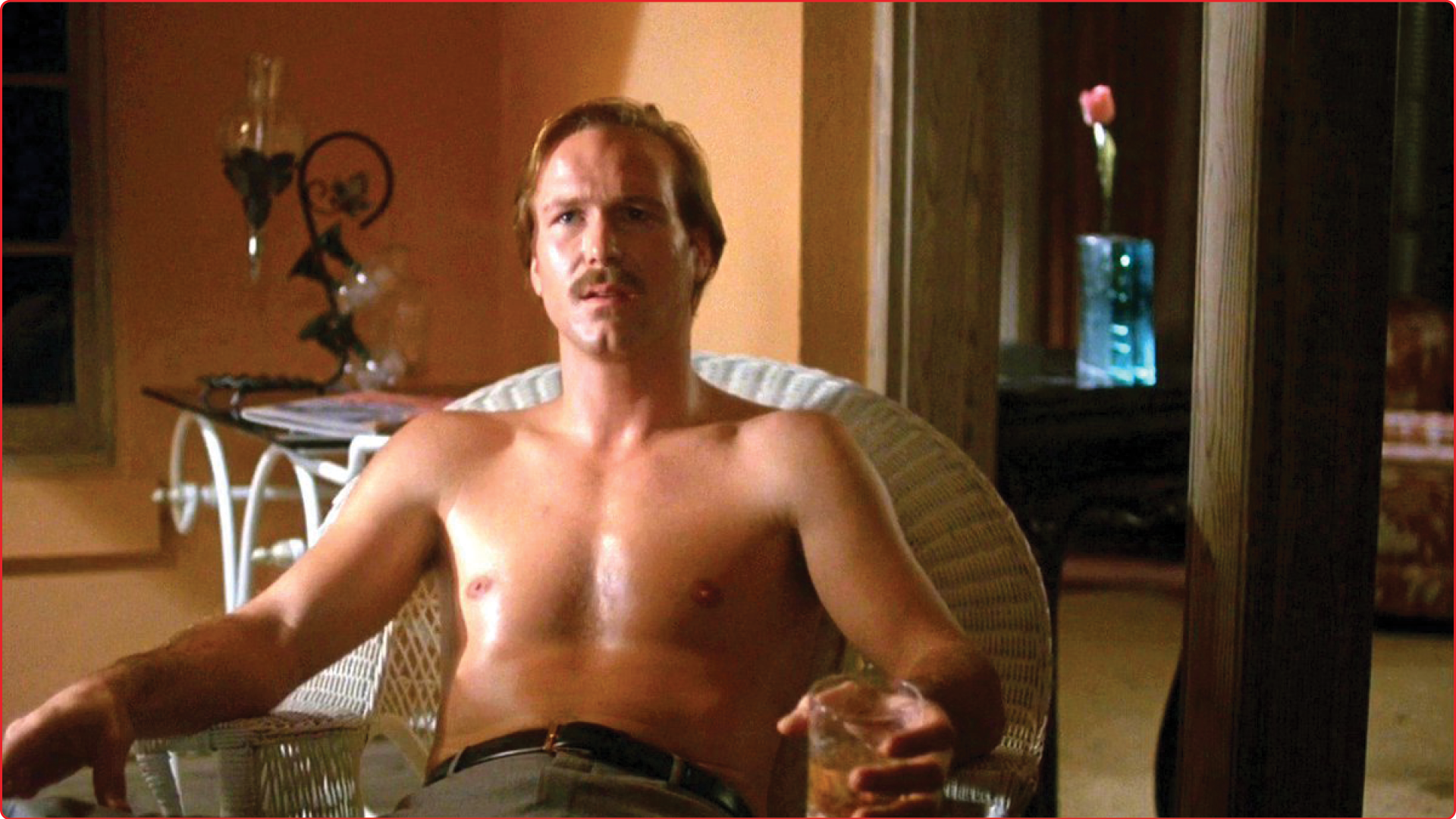 A sweaty, shirtless man with an 80s mustache sips scotch while appearing trapped in a white wicker chair. On his face is an expression of deep concern.