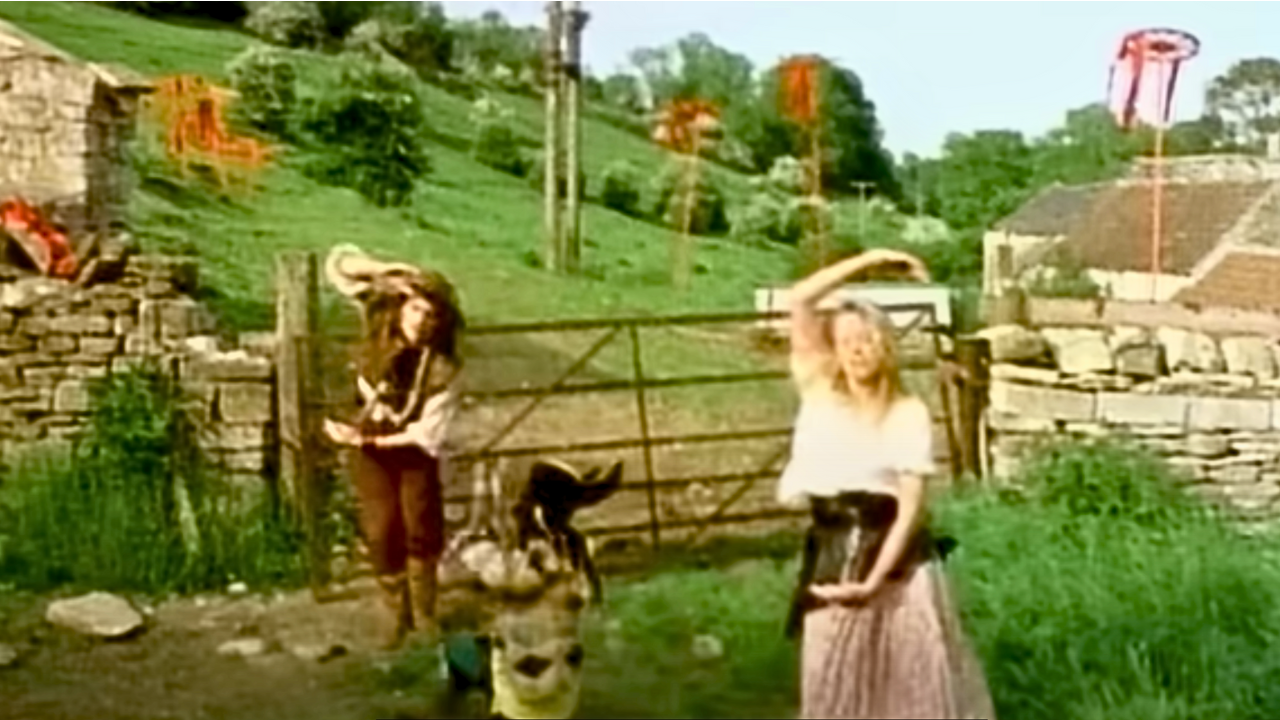 An image from the epically awful Safety Dance video. A man and a woman dressed for a Ren Fest make an S with their arms.