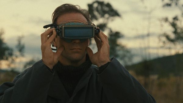  A savannah at dawn. A white man in his 40s wears a rectangular device over his eyes and is deeply engrossed with what he is seeing inside it.