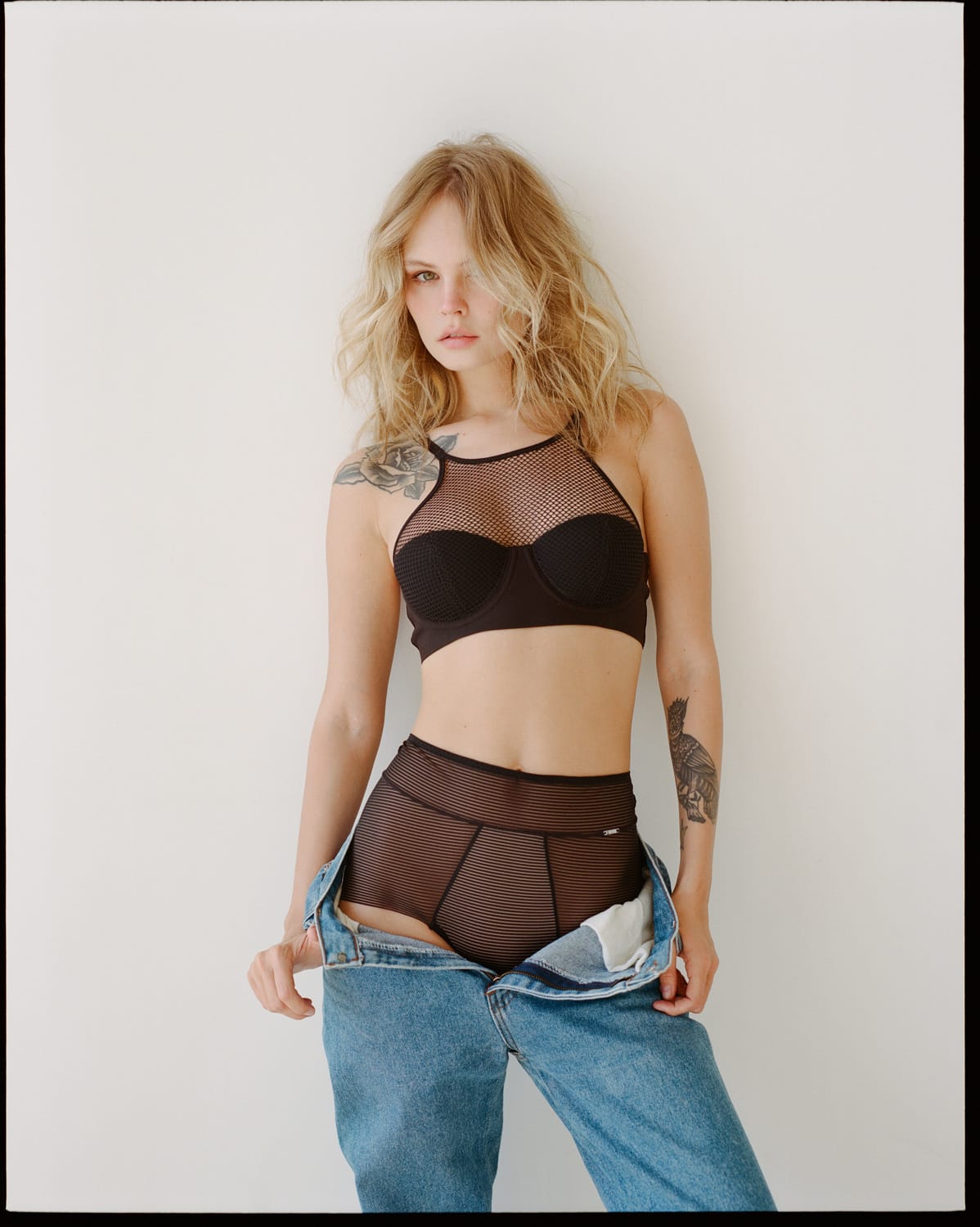Anastasiya Scheglova pulls down unbuttoned jeans to reveal black mesh briefs, hair tousled, photographed by Alina Korneeva.