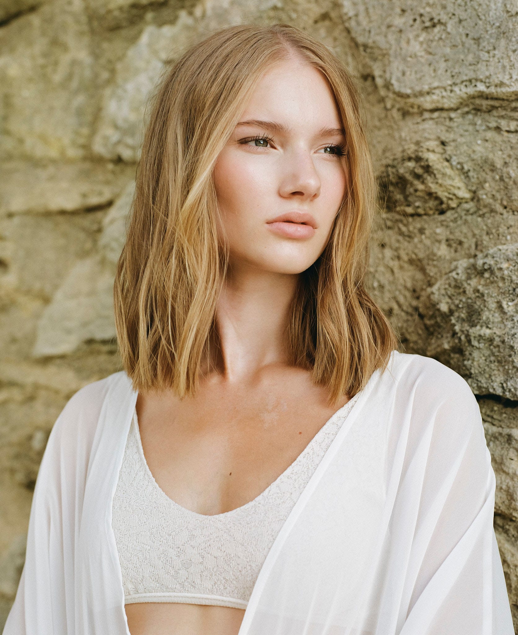 Marie Christin Behnisch looks off-camera against a stone wall in a white lace bralette and sheer coverup, photographed by Markus Wachter.