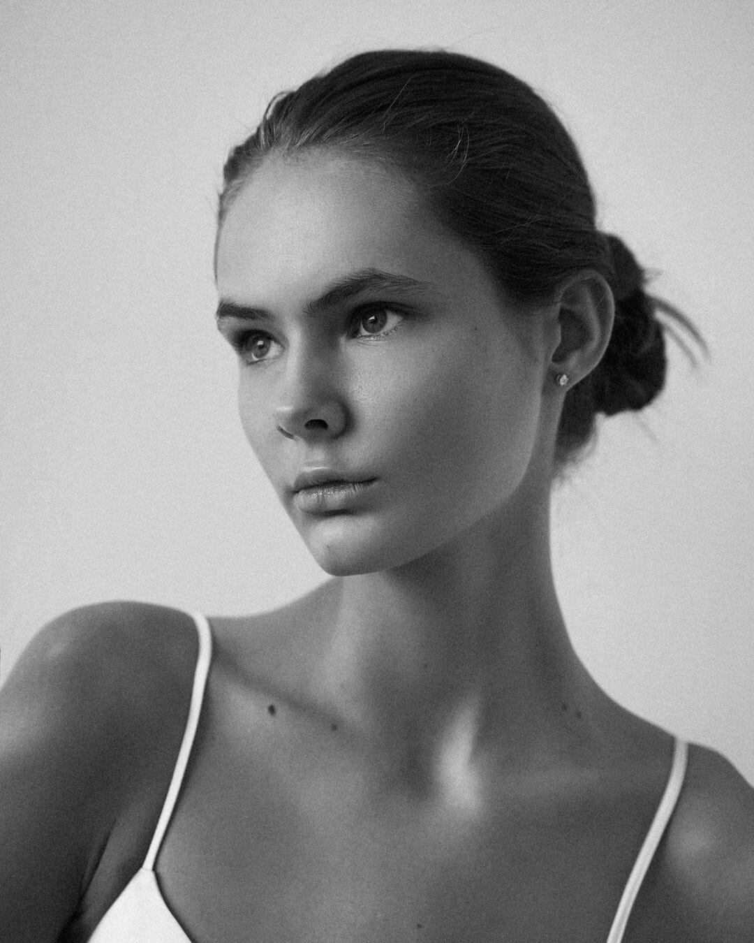 Close portrait of Olita Pimonova in a white camisole with hair pulled back, looking away from the camera, photographed by Maria Kudryavtseva.