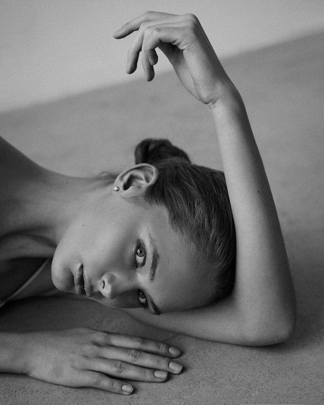 Olita Pimonova lies on the concrete floor with one hand raised, shot close on her face in black and white, photographed by Maria Kudryavtseva.