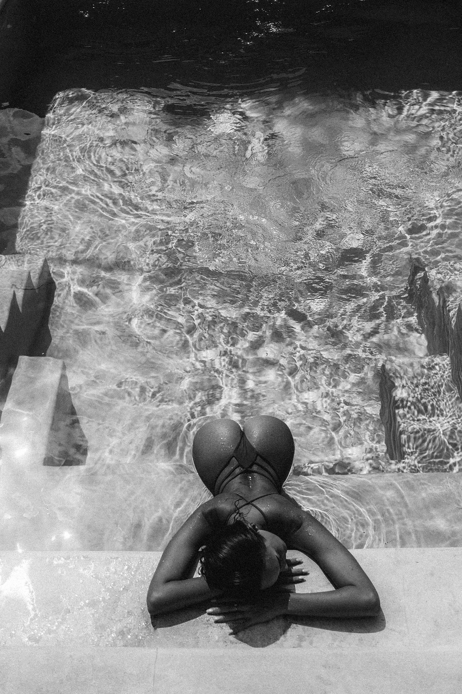 Sara Frazzetta rests her arms on the pool ledge, viewed from above with light refracting through the water, photographed by Tatyana Kudryashova.